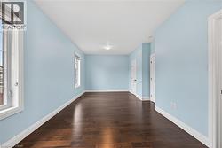 Spacious room featuring wood-finish flooring, light blue walls, multiple windows with blinds, white trim, and recessed lighting - 