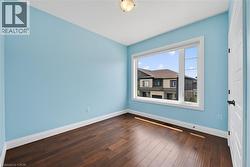 Bright interior space featuring a large window, dark wood-finish flooring, light blue painted walls, white baseboards, and a paneled interior door with matte black hardware - 