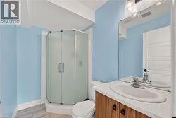 Bathroom featuring a corner shower with frosted glass enclosure, a white oval sink set into a wood-finish vanity with a white countertop, and light-colored tile flooring - 