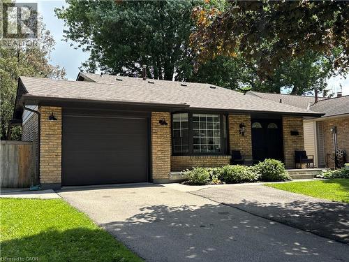 Brick facade residence featuring a dark garage door, paved driveway, mature landscaping, and a covered entry with dual dark doors - 39 Forestgate Drive, Hamilton, ON 