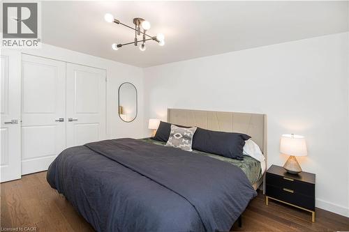 Bedroom featuring wood-finish flooring, a modern sputnik-style ceiling light, and white paneled doors - 39 Forestgate Drive, Hamilton, ON 