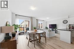 Open-concept living space featuring wood-finish flooring, a kitchen island with a dark countertop and undermount sink, a sliding glass door leading to an outdoor balcony, white walls, and recessed lig - 