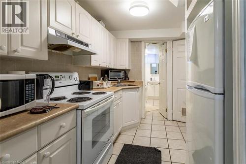 Efficient kitchen space featuring white cabinetry with traditional knobs, a built-in range hood, neutral-toned countertops, and square tile flooring - 17 Thorndale Street N, Hamilton, ON 