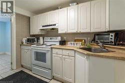 Kitchen featuring white cabinetry, light-toned countertops, a full-size range, and a double-basin sink - 