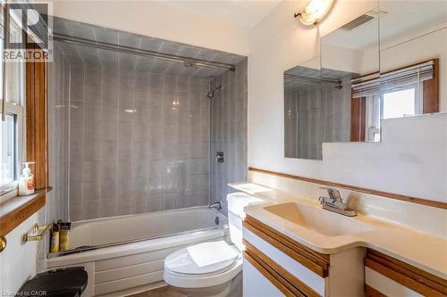 Bathroom featuring a bathtub with a shower, floor-to-ceiling gray tile surround, and an integrated shower curtain rod - 17 Thorndale Street N, Hamilton, ON 
