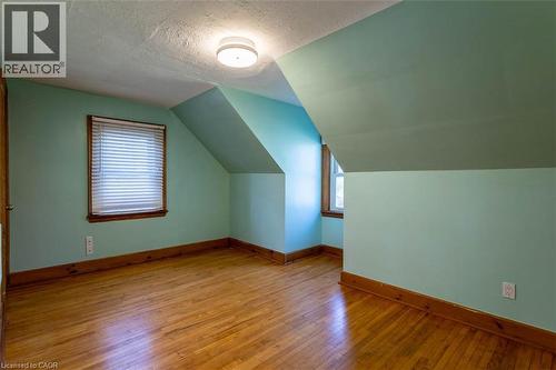 Room featuring wood-finish flooring, two windows with wood trim, and a ceiling-mounted light fixture - 17 Thorndale Street N, Hamilton, ON 