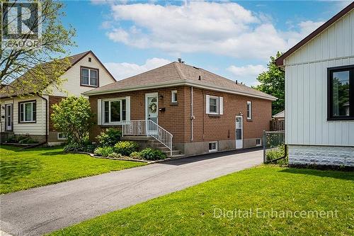 Brick exterior residence featuring a front entrance with white railings, a paved driveway, and established landscaping - 73 West 1St Street, Hamilton, ON 