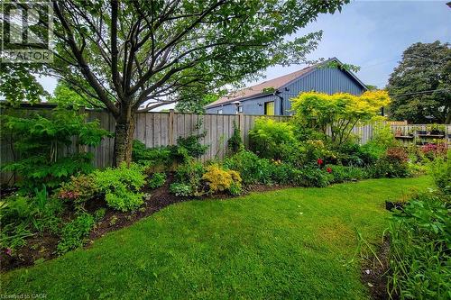 Expansive backyard featuring a manicured lawn, established garden beds with diverse foliage, and mature trees providing natural shading - 73 West 1St Street, Hamilton, ON 