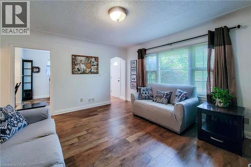 Living area featuring wood-finish flooring, a large window with blinds, and white painted walls - 73 West 1St Street, Hamilton, ON 