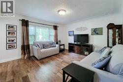 Living area featuring wood-finish flooring, white walls, and a large window with blinds - 
