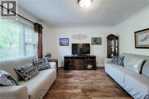 Spacious interior featuring wood-finish flooring, white painted walls, and a large window with blinds - 73 West 1St Street, Hamilton, ON 