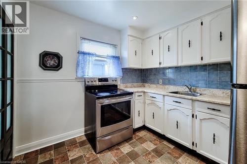 Kitchen featuring white cabinetry with dark hardware, a stainless steel range, a stainless steel sink, patterned tile flooring, and a blue tile backsplash - 73 West 1St Street, Hamilton, ON 