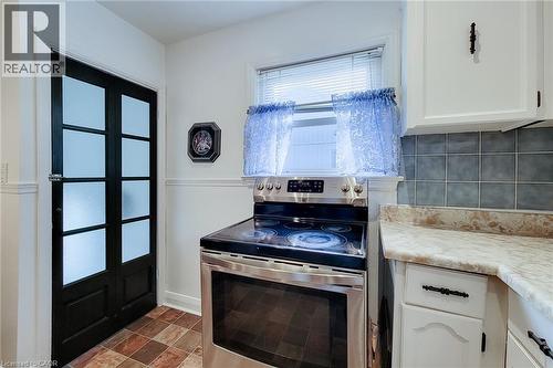 Kitchen featuring a stainless steel electric range, white cabinetry, and a black multi-pane door with frosted glass - 73 West 1St Street, Hamilton, ON 