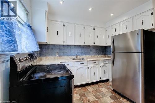 Kitchen featuring extensive white cabinetry with black hardware, a black electric range, and a stainless steel refrigerator - 73 West 1St Street, Hamilton, ON 