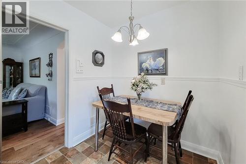 Dining area featuring a brushed nickel chandelier with frosted glass shades, a chair rail molding, and multi-toned square floor tiles - 73 West 1St Street, Hamilton, ON 