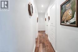 Hallway featuring wood-finish flooring, white walls, recessed lighting, and built-in white cabinetry with drawers and doors - 