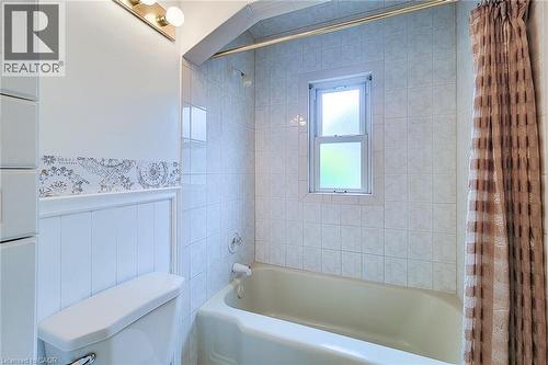 Bathroom featuring a white bathtub with an integrated shower, white tile surround, and an opaque window - 73 West 1St Street, Hamilton, ON 