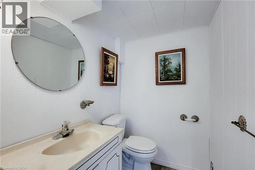 Bathroom featuring a white vanity with integrated sink, a single-handle faucet, an oval mirror, and white wall paneling - 73 West 1St Street, Hamilton, ON 