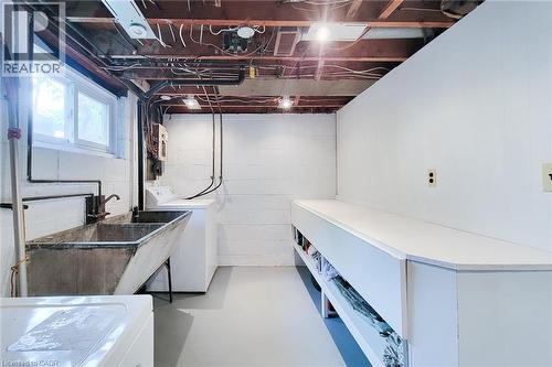 Basement utility area featuring a double-basin utility sink, exposed ceiling joists, and a built-in workbench with open shelving - 73 West 1St Street, Hamilton, ON 