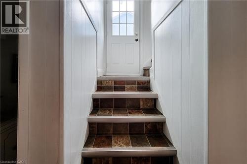 Staircase featuring multi-toned square tile treads with metal nosing, vertical paneling on side walls, and a white paneled door with a multi-pane window - 73 West 1St Street, Hamilton, ON 