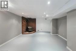 Spacious room featuring a brick-clad fireplace surround with a dark metal stove, light painted walls, white baseboards, and light gray flooring, illuminated by recessed ceiling lighting. - 