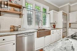 Kitchen featuring a copper farmhouse sink, stainless steel dishwasher, white cabinetry with dark hardware, stone countertops, and a patterned tile backsplash - 
