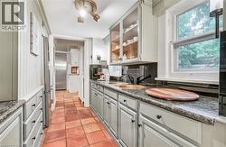 Galley kitchen featuring terracotta tile flooring, granite countertops, painted cabinetry, and glass-front upper cabinets - 