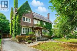 Brick exterior with extensive green climbing vine, multiple chimneys, a covered entryway, and bay windows - 