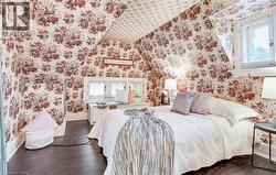 Attic room featuring sloped ceilings, floral patterned wallpaper, wood-finish flooring, a built-in window seat, and white trim - 