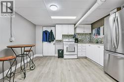 Kitchen area featuring white cabinetry, light-toned backsplash, and wood-finish flooring - 