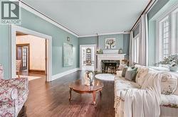 Living room featuring wood-finish flooring, a white mantel fireplace with a dark stone surround, multiple large windows, and crown molding - 