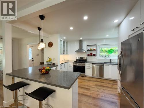 Modern kitchen featuring a breakfast bar with stone-finish countertop, stainless steel appliances, white subway tile backsplash, recessed lighting, and wood-finish flooring - 1324 Bodley Road, Mississauga, ON 