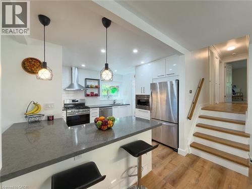 Modern kitchen featuring a grey stone-finish countertop island, stainless steel appliances, white cabinetry, and wood-finish flooring - 1324 Bodley Road, Mississauga, ON 