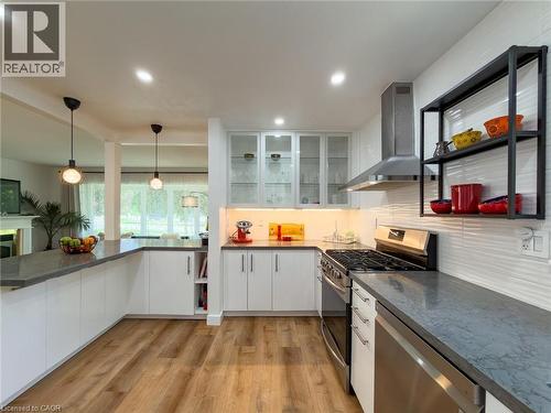 Contemporary kitchen featuring wood-finish flooring, white cabinetry, integrated stainless steel appliances, a range hood, and a textured white tile backsplash - 1324 Bodley Road, Mississauga, ON 