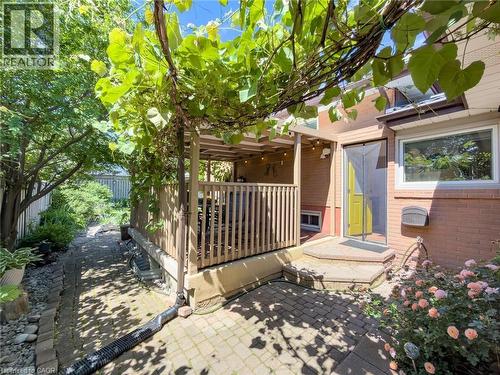 Outdoor patio area featuring a covered deck with wooden railings, a yellow-painted exterior door, and a brick paver patio - 1324 Bodley Road, Mississauga, ON 