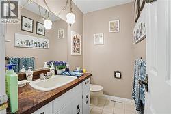 Bathroom featuring a white vanity with dark-finish countertop and integrated sink, white base cabinetry with dark hardware, a toilet, and light-toned floor tiling - 
