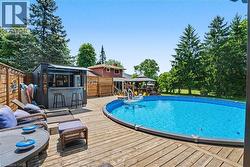 Expansive outdoor living area featuring a large swimming pool, a substantial wood deck, a built-in outdoor bar, and mature perimeter trees - 