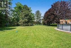 Expansive lawn area featuring mature trees and an above-ground pool with surrounding wooden privacy screening - 