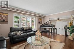 Spacious living area featuring rich wood-finish flooring, crown molding, and plantation shutters - 