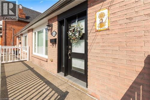 Brick exterior featuring an entry door with frosted glass panels, an exterior wall sconce, and a white framed window. - 202 Ray Street N, Hamilton, ON - Outdoor With Exterior