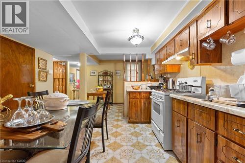 Kitchen and dining area featuring wood cabinetry, white appliances, patterned floor tile, and a drop ceiling. - 202 Ray Street N, Hamilton, ON - Indoor Photo Showing Kitchen