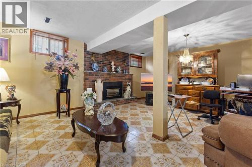 Spacious recreation room featuring patterned tile flooring, a brick fireplace with mantel, and a prominent support column. - 202 Ray Street N, Hamilton, ON - Indoor With Fireplace