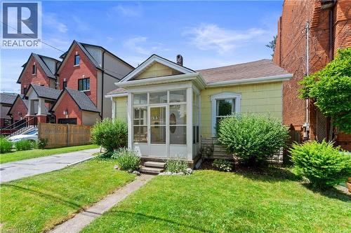 Yellow-sided residence featuring a screened-in front porch, a gabled roofline, and a paved driveway. - 193 Locke Street N, Hamilton, ON - Outdoor With Facade