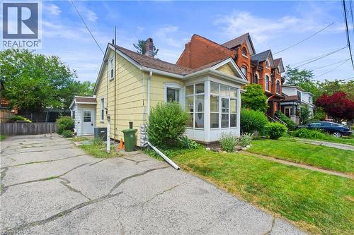 Yellow-sided residence featuring a screened-in front porch, a gabled roofline, and a paved driveway. - 193 Locke Street N, Hamilton, ON - Outdoor