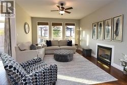 Living area featuring wood-finish flooring, an inset fireplace with a white mantel, and a ceiling fan with integrated lighting - 
