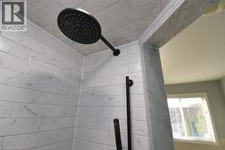 Shower enclosure featuring white subway tile with subtle grey veining, a matte black rainfall showerhead, and a matte black handheld shower - 