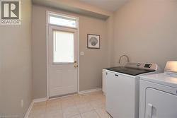 Dedicated laundry area featuring ceramic tile flooring, a white exterior door with an overhead transom window, and neutral wall tones - 