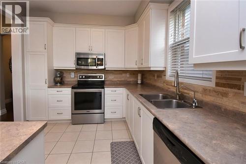 Kitchen featuring white cabinetry, stone-look countertops, stainless steel appliances, a stacked stone backsplash, and tile flooring - 188 Hunter Way, Brantford, ON - Indoor Photo Showing Kitchen With Double Sink