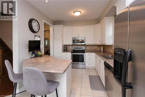 Kitchen featuring white cabinetry, stainless steel appliances, a breakfast bar, stone-look countertops, and tile flooring - 188 Hunter Way, Brantford, ON - Indoor