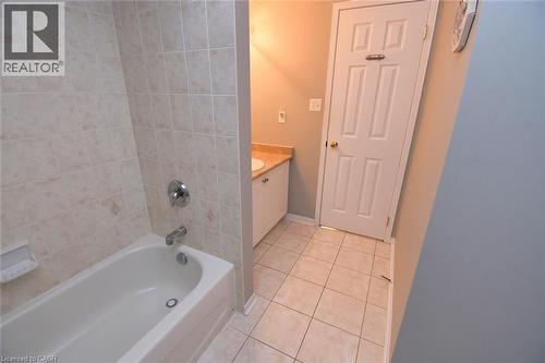 Bathroom featuring a white bathtub with chrome fixtures, tiled surround, vanity with a light-colored countertop, and a paneled door - 188 Hunter Way, Brantford, ON - Indoor Photo Showing Bathroom